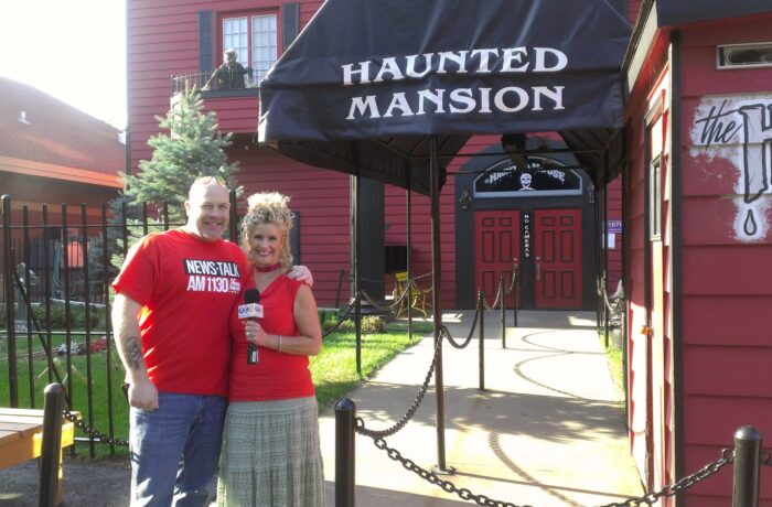 Dave Schrader & Jodi in front of the not so haunted house at the fair